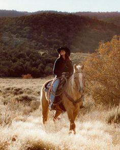 a woman riding on the back of a brown horse in a field next to trees