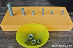 a yellow bowl with screws in it sitting next to a wooden peg board on the ground