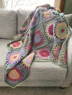 a crocheted granny blanket is sitting on a couch next to a pillow and window