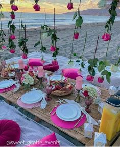 a table set up with plates and flowers on the beach