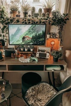 a computer desk with plants and candles on it in front of a large screen tv