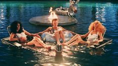 four women sitting on rafts in the water with zebra statue behind them at night