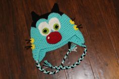 a blue crocheted hat with eyes and horns on top of a wooden floor