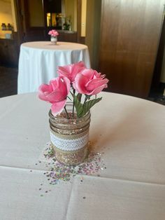 some pink flowers are in a mason jar on a white table cloth with confetti sprinkles