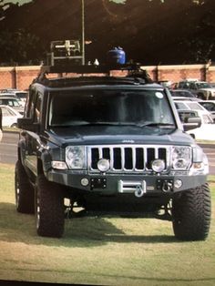 a black jeep parked on top of a lush green field next to a parking lot