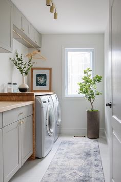 a washer and dryer in a white laundry room with plants on the counter