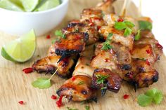 chicken skewers with garnishes on a cutting board next to a bowl of lime wedges