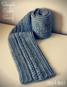 a blue knitted scarf sitting on top of a white table next to a roll of yarn