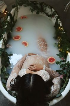 a woman laying down in a bath filled with water surrounded by fruits and greenery