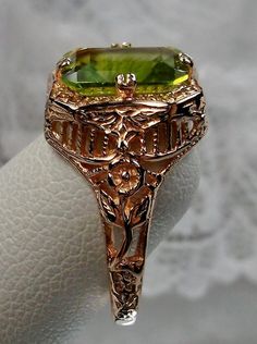 Natural Green Peridot 10k or 14k Rose Gold RingLovely Rectangle Design#D148 Make heads turn and stand out with this gorgeous piece of jewelry! This Edwardian reproduction filigree ring is made from rose gold and features an emerald cut high quality natural green Peridot gemstone measuring 9mm by 7mm. From the beautiful intricate floral daisy design to the inside of the band marked 10K or 14K for gold – this ring will take your look to the next level! Look no further than this exquisite vintage-i Yellow Gold Peridot Jewelry With Emerald Cut, Victorian 14k Stamped Green Jewelry, Gold Peridot Jewelry With Emerald Cut, Elegant Rectangular Peridot Rings, Emerald Cut Peridot Jewelry For Formal Events, Emerald Cut Peridot Jewelry For Formal Occasions, Formal Emerald Cut Peridot Jewelry, Art Deco Green Octagon Jewelry, Elegant Rectangular Peridot Jewelry