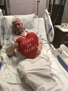 an older man laying in a hospital bed holding a heart shaped pillow with the words i heart to heart written on it