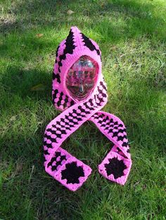 a pink and black crocheted object laying in the grass with its hood up