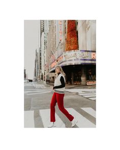 a woman walking across a cross walk in the middle of a city with tall buildings