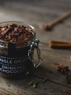 a glass jar filled with chocolate chips on top of a wooden table next to cinnamon sticks