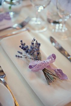 the napkins are decorated with lavender flowers and silverware on top of white table cloth