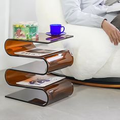 a person sitting in a chair with a coffee cup and magazine rack on the floor