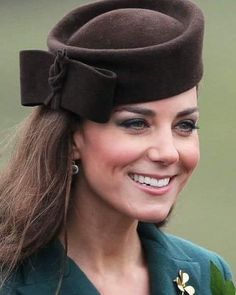 a smiling woman wearing a brown hat and green jacket with a flower on the side