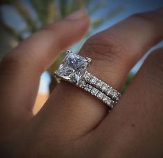 a woman's hand with a diamond ring and wedding band on top of it