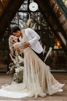 a bride and groom kissing in front of a wooden structure with flowers on the floor