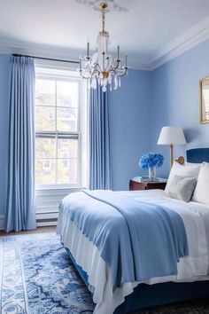 a blue and white bedroom with chandelier, bed, rug and window in the background