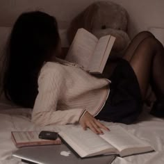 a woman laying in bed reading a book and holding an apple laptop next to her