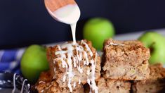 a spoon drizzling white icing over some apple dessert bars on a plate