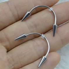 two small silver earrings are shown on someone's hand, one is in the shape of an arrow