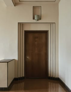 an empty hallway with a wooden door and mirror above the doorway, in front of a white wall