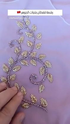 someone is stitching something with gold thread on a pink shirt that has leaves and vines on it