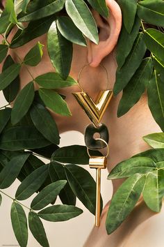 a close up of a person's face with leaves around her and a gold key hanging from the neck