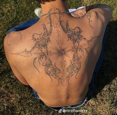 the back of a person with tattoos on their body sitting in grass and looking down