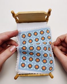 two hands are holding a small piece of crocheted cloth with flowers on it