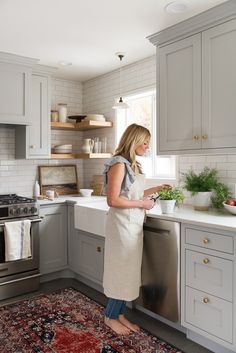 a woman in an apron is standing at the kitchen counter and looking at her phone