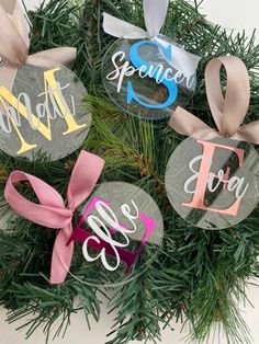 four ornaments are hanging on the tree with ribbons and bows around them that spell out names