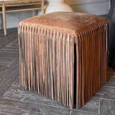 a brown leather stool with fringes on the top and bottom, in front of a chair