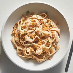 a white bowl filled with pasta on top of a table next to utensils