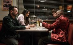 three people sitting at a table in a restaurant and one person is holding something up to another man's hand