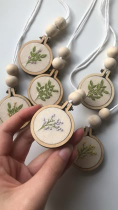 a hand is holding an embroidered necklace with lavenders and green leaves on the beads