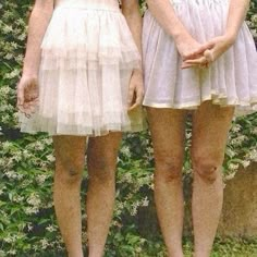 two young women standing next to each other in front of a wall covered with flowers