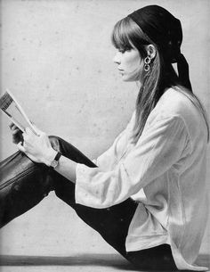 a woman sitting on the floor reading a book with her legs crossed and wearing black pants