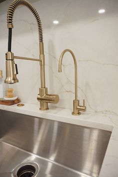 a kitchen sink with a brass faucet next to a stainless steel drainer