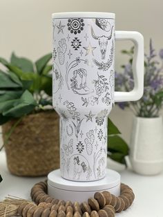 a white coffee mug sitting on top of a table next to some beads and plants