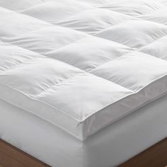 an image of a white mattress topper on a wooden bed frame with no sheets