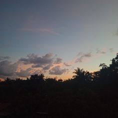 the sun is setting behind some trees and clouds in the sky, with only one cloud visible