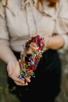 a woman is holding a flower crown in her hands while wearing a button up shirt