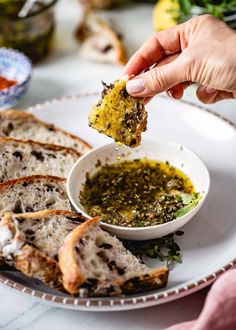 a person dipping something into a small bowl on top of a white plate with bread