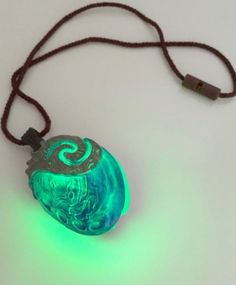 a necklace with a glowing green ball on it's side and a black cord attached to it