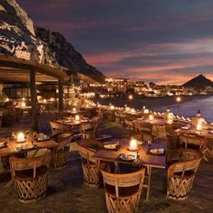 an outdoor dining area overlooking the ocean at night with lit candles on tables and chairs