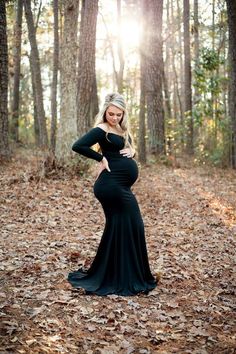 a pregnant woman standing in the woods wearing a long black dress with her hands on her hips