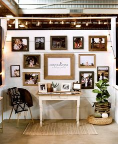 a room with many pictures on the wall and a desk in front of it that has a potted plant next to it